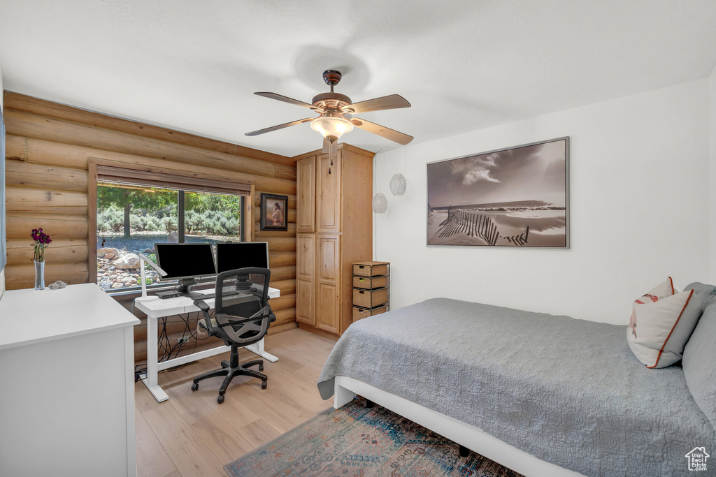 Bedroom with ceiling fan, light hardwood / wood-style floors, and log walls