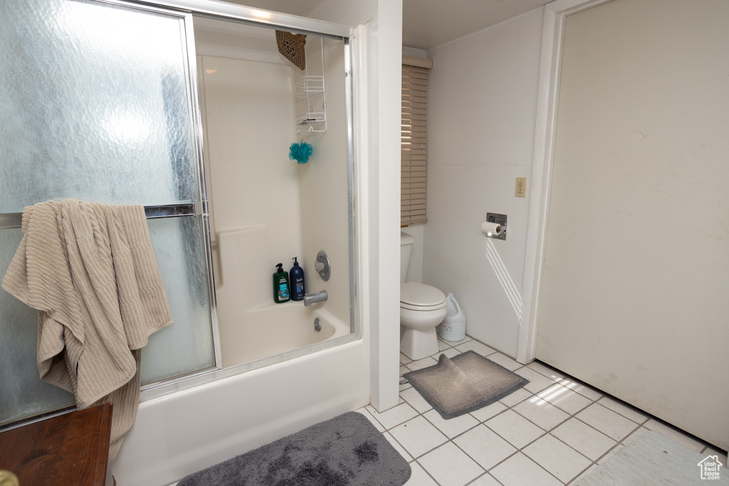 Bathroom featuring tile flooring, combined bath / shower with glass door, and toilet