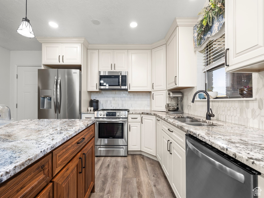 Kitchen with stainless steel appliances, backsplash, hardwood / wood-style floors, sink, and pendant lighting