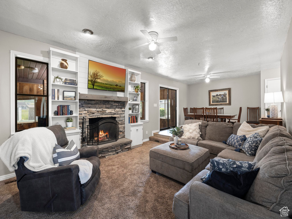 Living room featuring a stone fireplace, ceiling fan, a textured ceiling, and carpet flooring