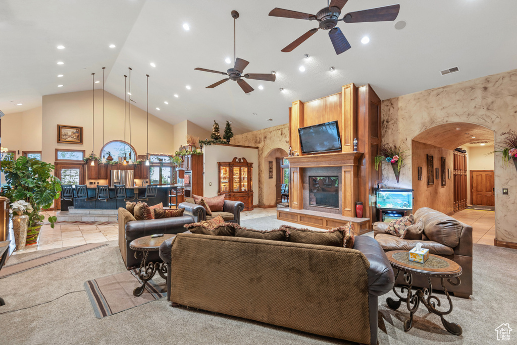 Living room featuring high vaulted ceiling, ceiling fan, a large fireplace, and light colored carpet