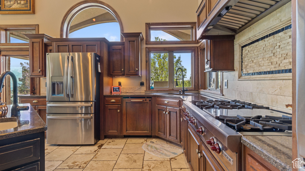 Kitchen featuring custom exhaust hood, stainless steel fridge with ice dispenser, light tile patterned floors, range, and sink