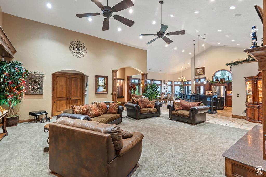 Carpeted living room featuring high vaulted ceiling and ceiling fan with notable chandelier