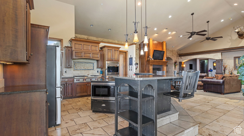 Kitchen with a breakfast bar area, pendant lighting, appliances with stainless steel finishes, a center island, and ceiling fan