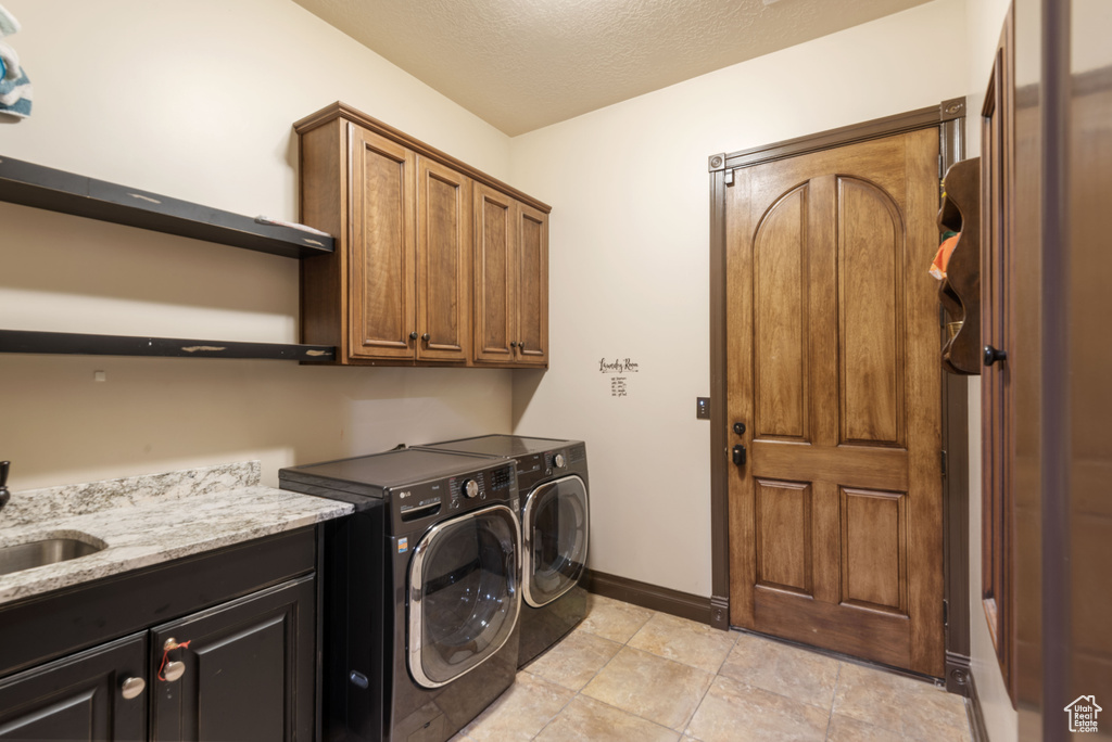 Washroom with cabinets, a textured ceiling, light tile floors, and washing machine and dryer