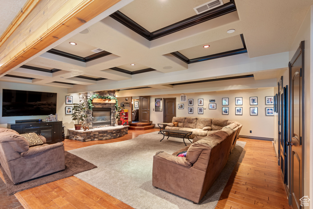 Living room with a stone fireplace, beam ceiling, coffered ceiling, and light hardwood / wood-style flooring