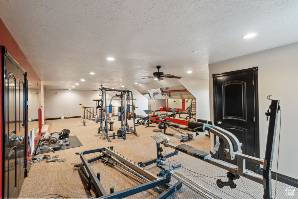 Workout room featuring a textured ceiling, lofted ceiling, ceiling fan, and light colored carpet