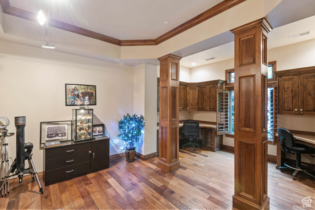 Office space featuring ornate columns, hardwood / wood-style flooring, and built in desk