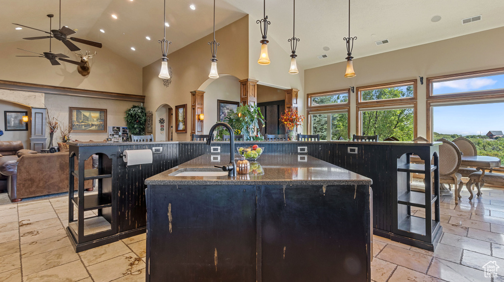 Kitchen featuring pendant lighting, light tile patterned floors, dark stone countertops, an island with sink, and ceiling fan