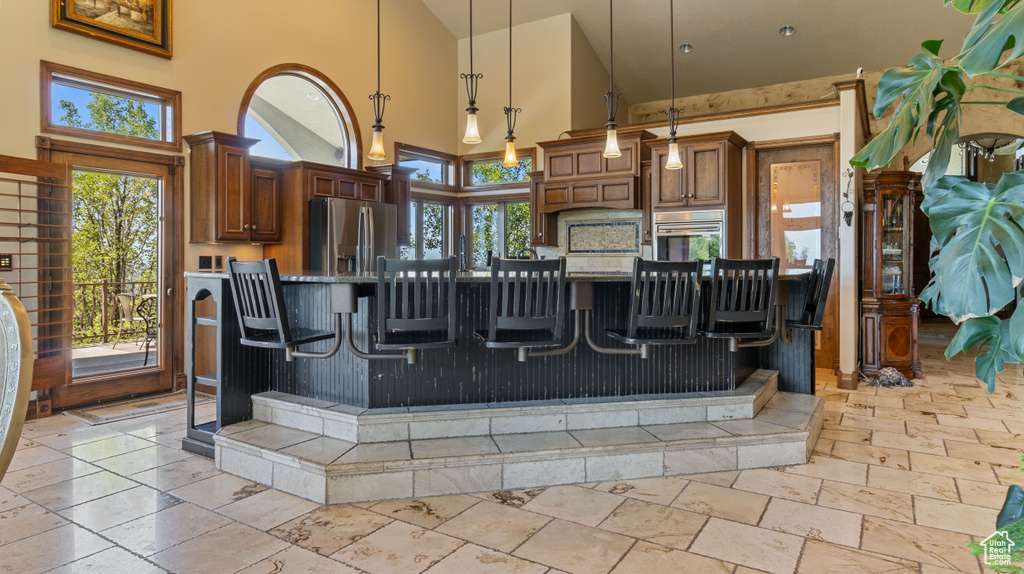 Kitchen with appliances with stainless steel finishes, high vaulted ceiling, light tile patterned floors, decorative light fixtures, and a breakfast bar area