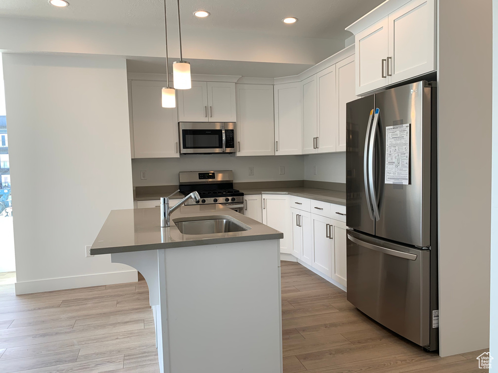 Kitchen with decorative light fixtures, light hardwood / wood-style flooring, stainless steel appliances, a kitchen breakfast bar, and white cabinets