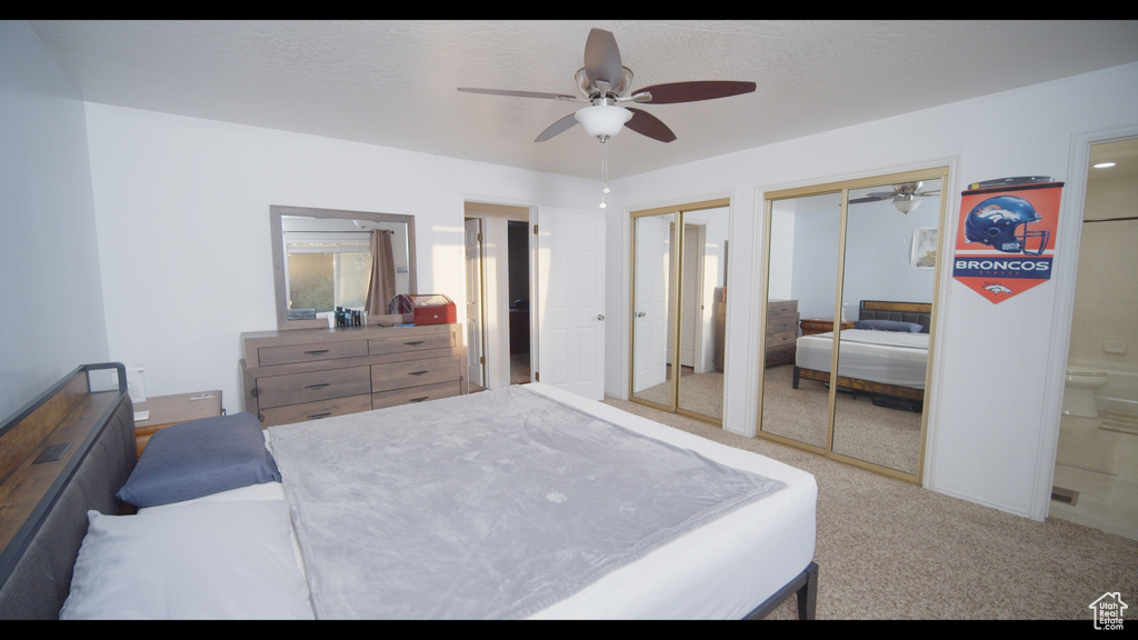 Carpeted bedroom featuring multiple closets, ensuite bathroom, and ceiling fan