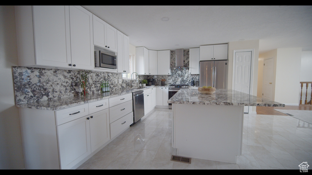 Kitchen with a kitchen island, stainless steel appliances, white cabinets, wall chimney exhaust hood, and tasteful backsplash