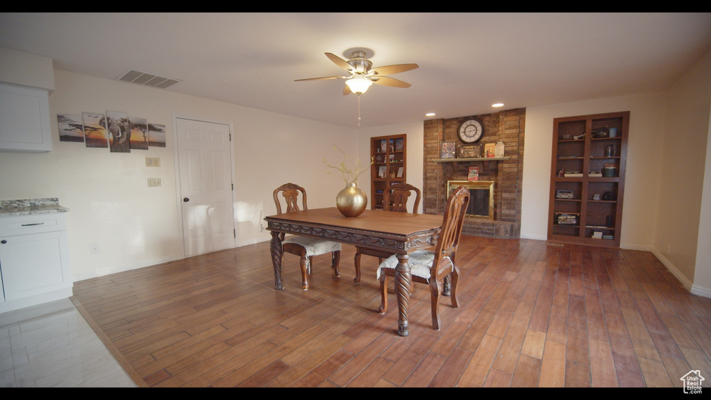 Dining space featuring brick wall, ceiling fan, hardwood / wood-style flooring, and a fireplace