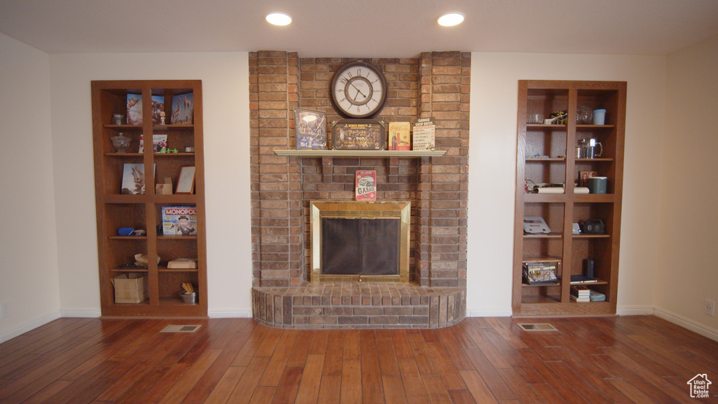 Unfurnished living room featuring brick wall, a brick fireplace, and hardwood / wood-style floors