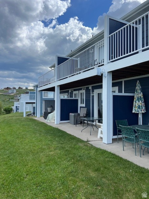 Rear view of house featuring a patio, a balcony, and a lawn