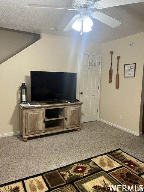 Carpeted living room featuring ceiling fan and a textured ceiling