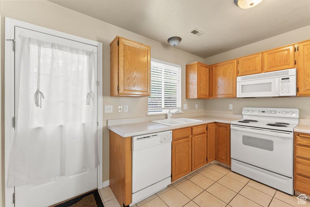 Kitchen featuring sink, white appliances, and light tile floors