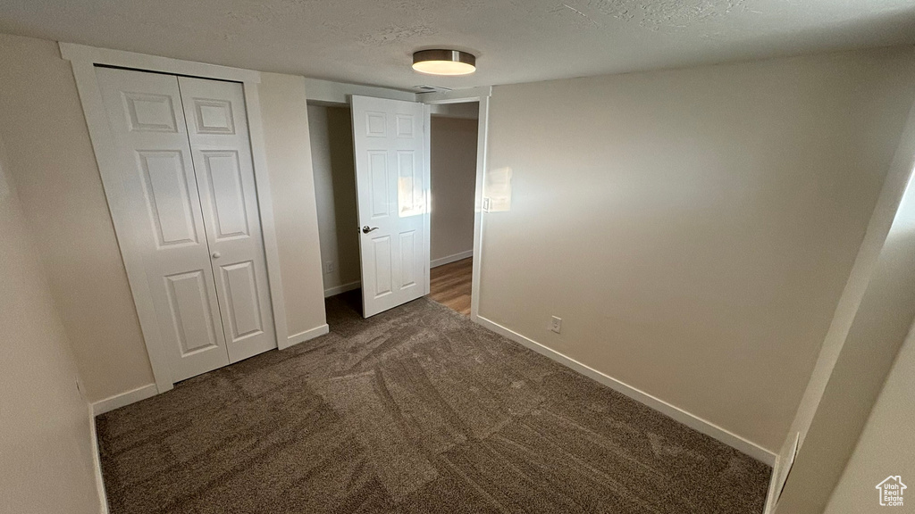 Unfurnished bedroom with a textured ceiling, a closet, and dark carpet