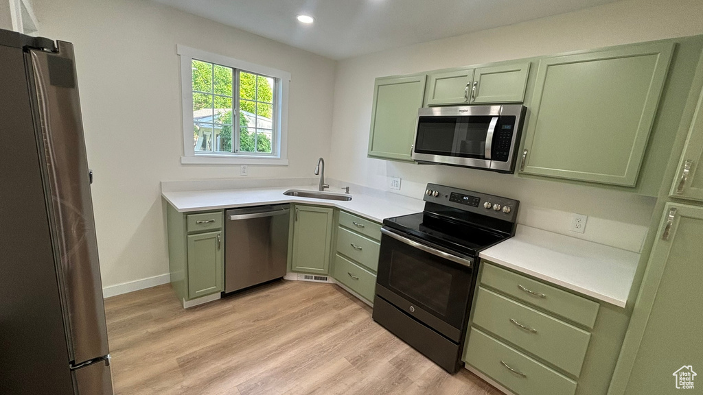 Kitchen featuring green cabinetry, appliances with stainless steel finishes, sink, and light wood-type flooring