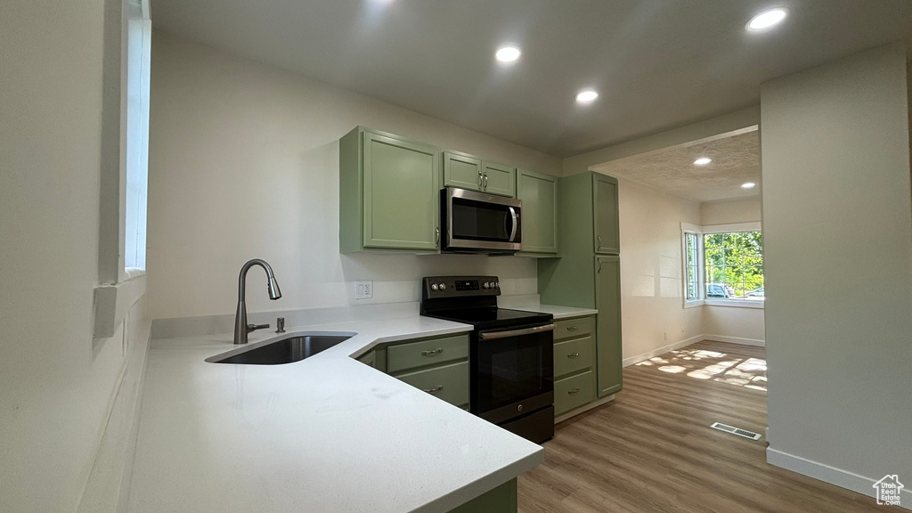 Kitchen with electric range, sink, green cabinets, and hardwood / wood-style flooring