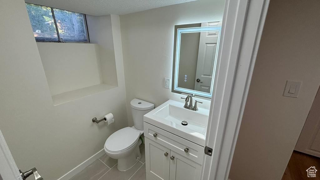 Bathroom with a textured ceiling, tile flooring, toilet, and vanity with extensive cabinet space