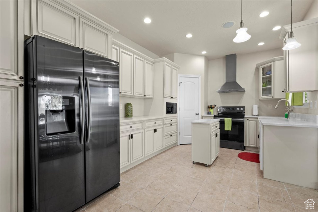 Kitchen featuring wall chimney range hood, hanging light fixtures, a kitchen island, black appliances, and white cabinets