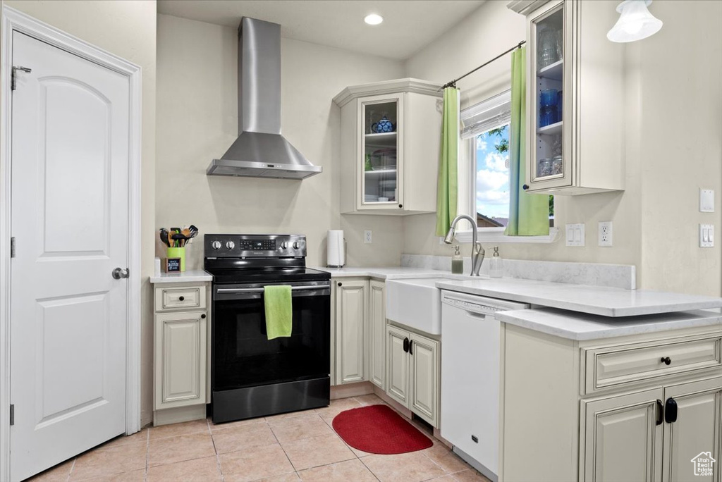 Kitchen with wall chimney range hood, light tile flooring, range with electric stovetop, white dishwasher, and sink