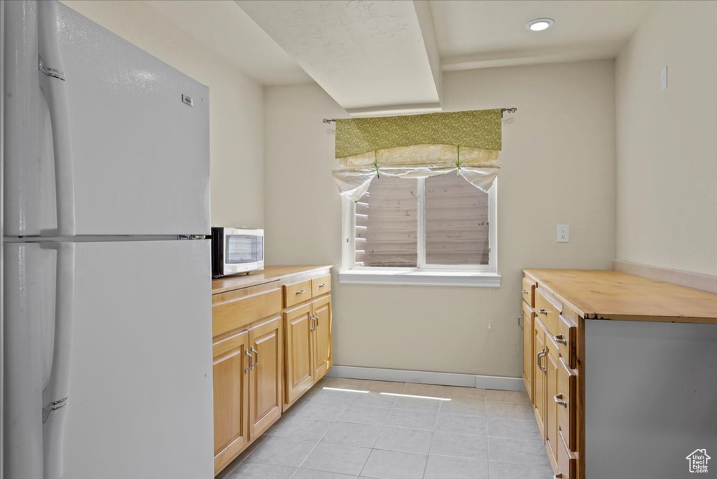 Kitchen with white fridge, wood counters, and light tile floors