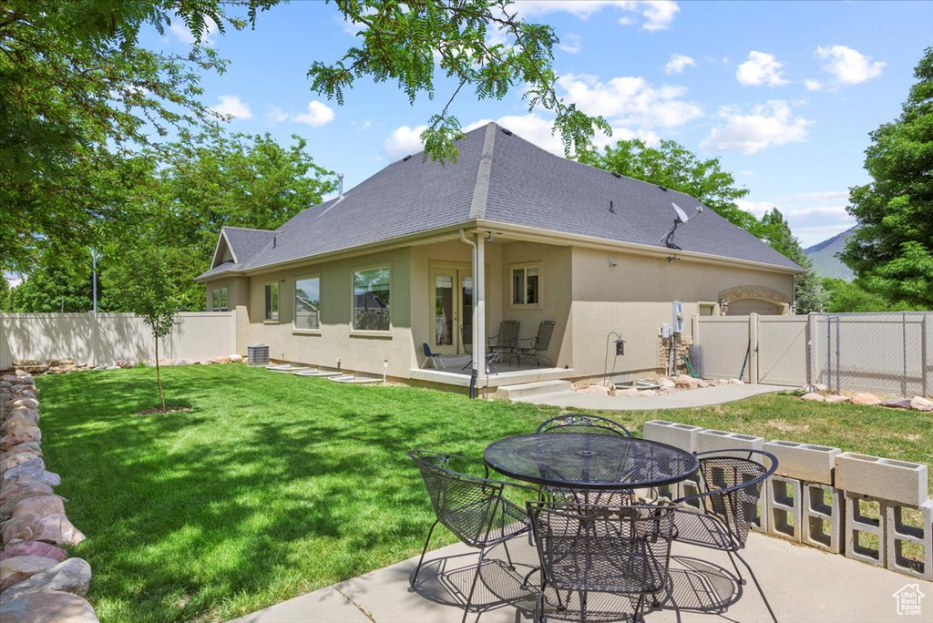 Rear view of property with a patio area, central air condition unit, and a lawn