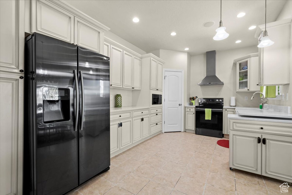 Kitchen featuring wall chimney range hood, black refrigerator with ice dispenser, hanging light fixtures, range with electric stovetop, and white cabinetry