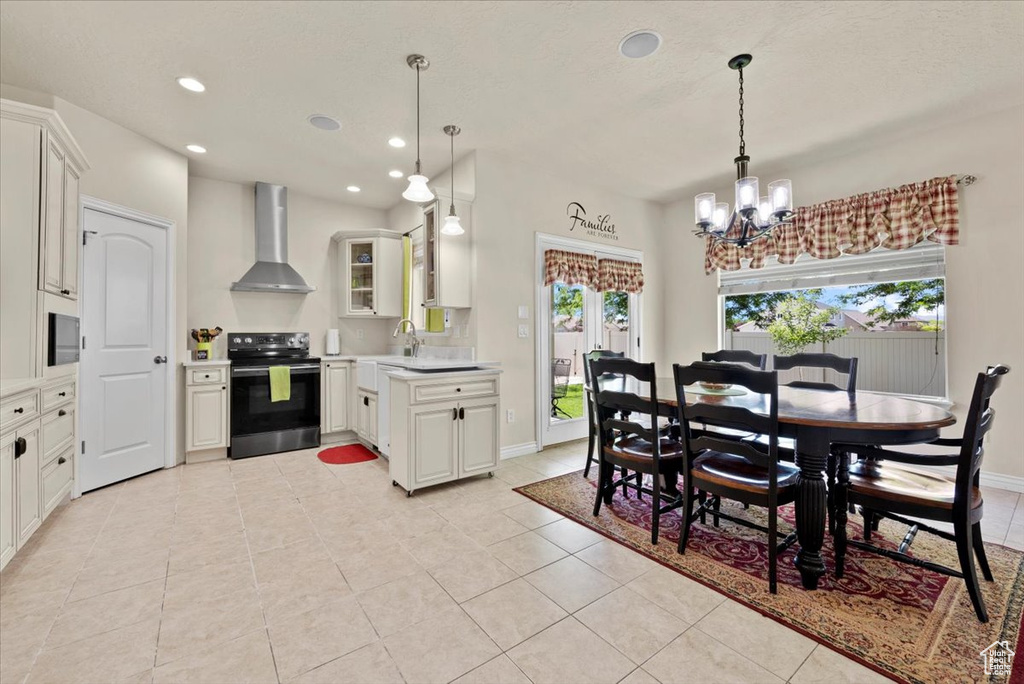 Kitchen with wall chimney range hood, hanging light fixtures, white cabinetry, range with electric stovetop, and light tile floors