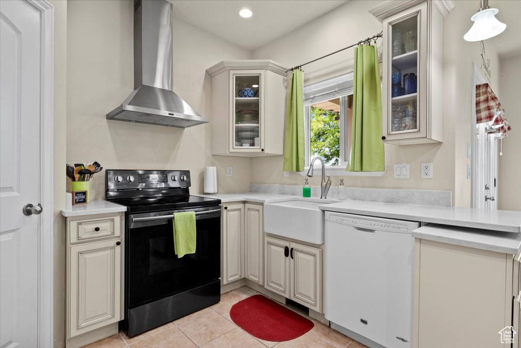 Kitchen featuring dishwasher, light tile floors, wall chimney range hood, sink, and range with electric stovetop