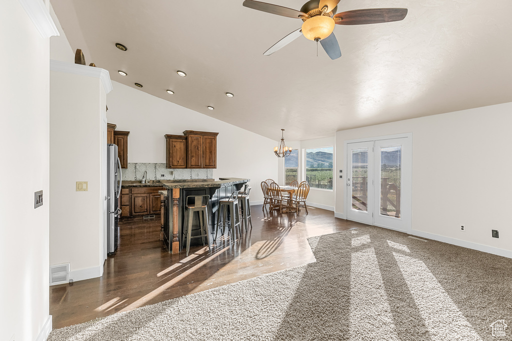 Kitchen with vaulted ceiling, a kitchen island, tasteful backsplash, stainless steel fridge, and wood-type flooring