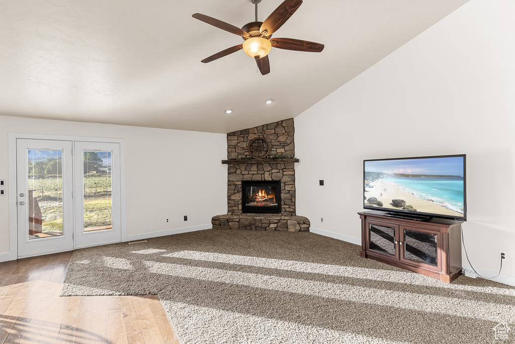 Carpeted living room with vaulted ceiling, a stone fireplace, and ceiling fan