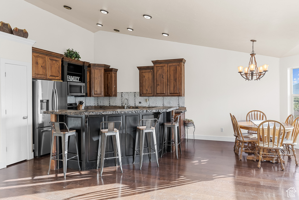 Kitchen featuring a kitchen breakfast bar, dark hardwood / wood-style flooring, stainless steel appliances, backsplash, and a notable chandelier