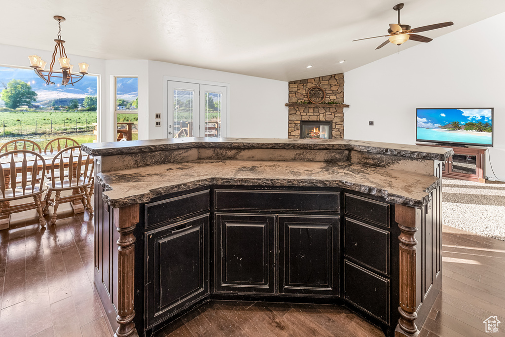 Kitchen with hanging light fixtures, a kitchen island, dark hardwood / wood-style floors, a stone fireplace, and vaulted ceiling