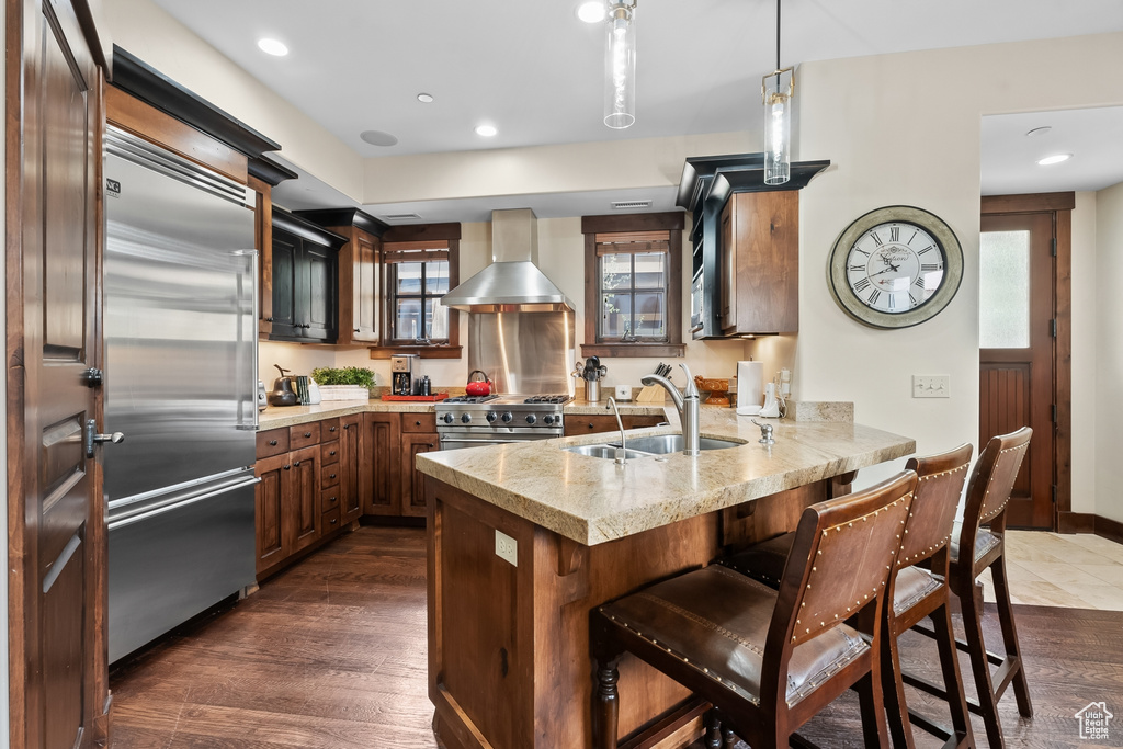 Kitchen featuring premium appliances, kitchen peninsula, hardwood / wood-style floors, wall chimney exhaust hood, and sink