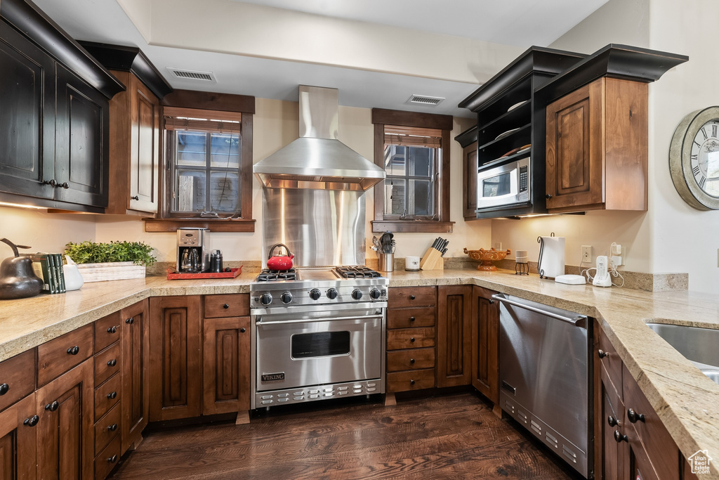 Kitchen featuring dark wood-type flooring, appliances with stainless steel finishes, light stone countertops, and wall chimney exhaust hood