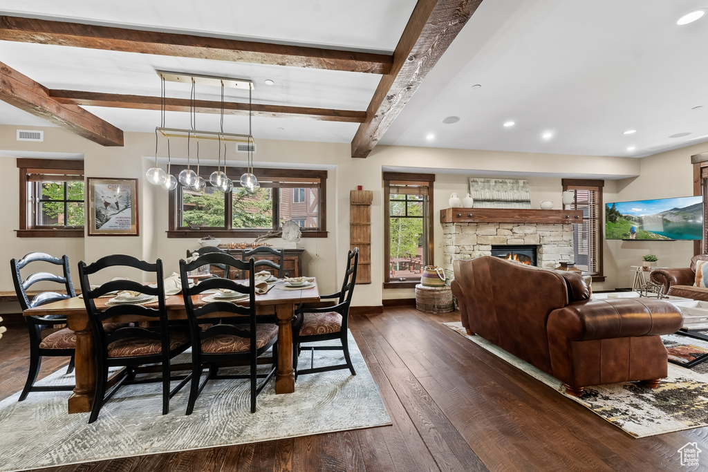 Dining space with a stone fireplace, a healthy amount of sunlight, beamed ceiling, and dark hardwood / wood-style flooring