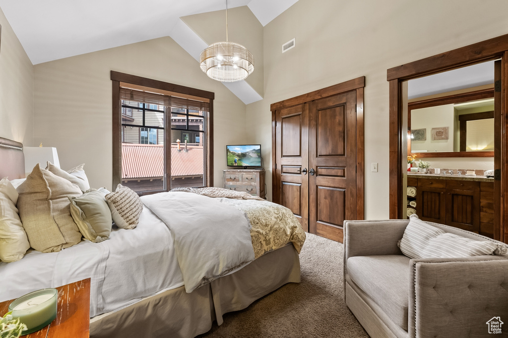 Carpeted bedroom featuring an inviting chandelier, connected bathroom, and lofted ceiling