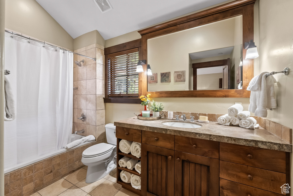 Full bathroom with shower / tub combo with curtain, tile floors, lofted ceiling, toilet, and vanity