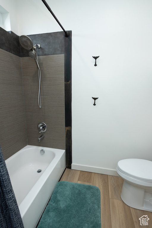 Bathroom with tiled shower / bath combo, wood-type flooring, and toilet