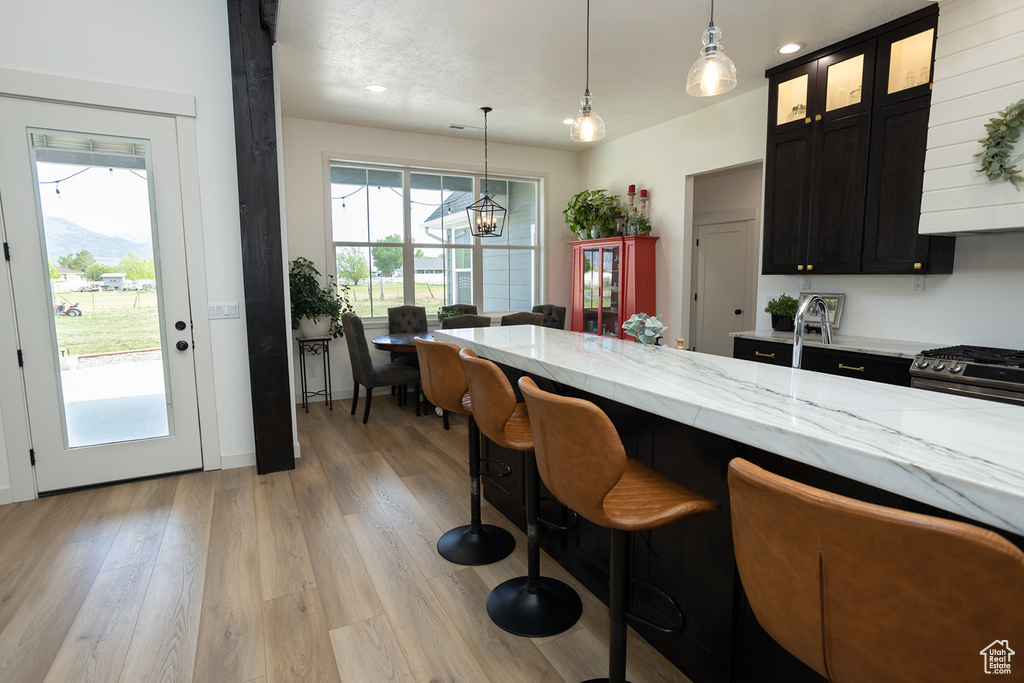 Kitchen with stainless steel range with gas stovetop, hanging light fixtures, light stone countertops, light hardwood / wood-style flooring, and exhaust hood