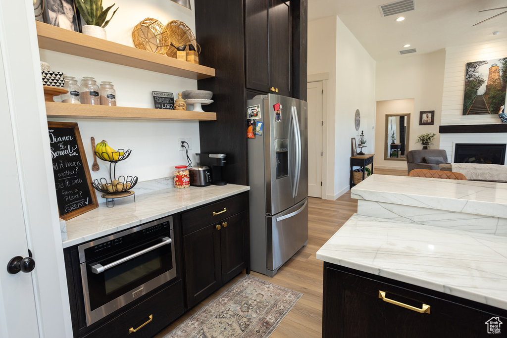 Kitchen with light stone counters, appliances with stainless steel finishes, light hardwood / wood-style floors, and a fireplace