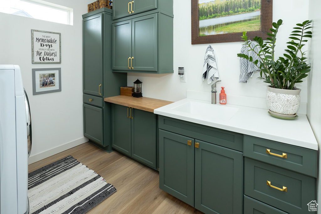 Kitchen featuring sink, green cabinetry, washer / clothes dryer, and light hardwood / wood-style flooring