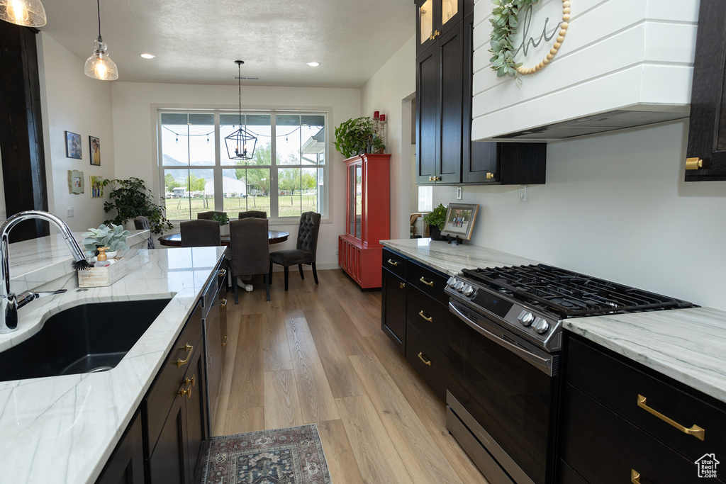 Kitchen featuring custom range hood, stainless steel appliances, light wood-type flooring, sink, and pendant lighting