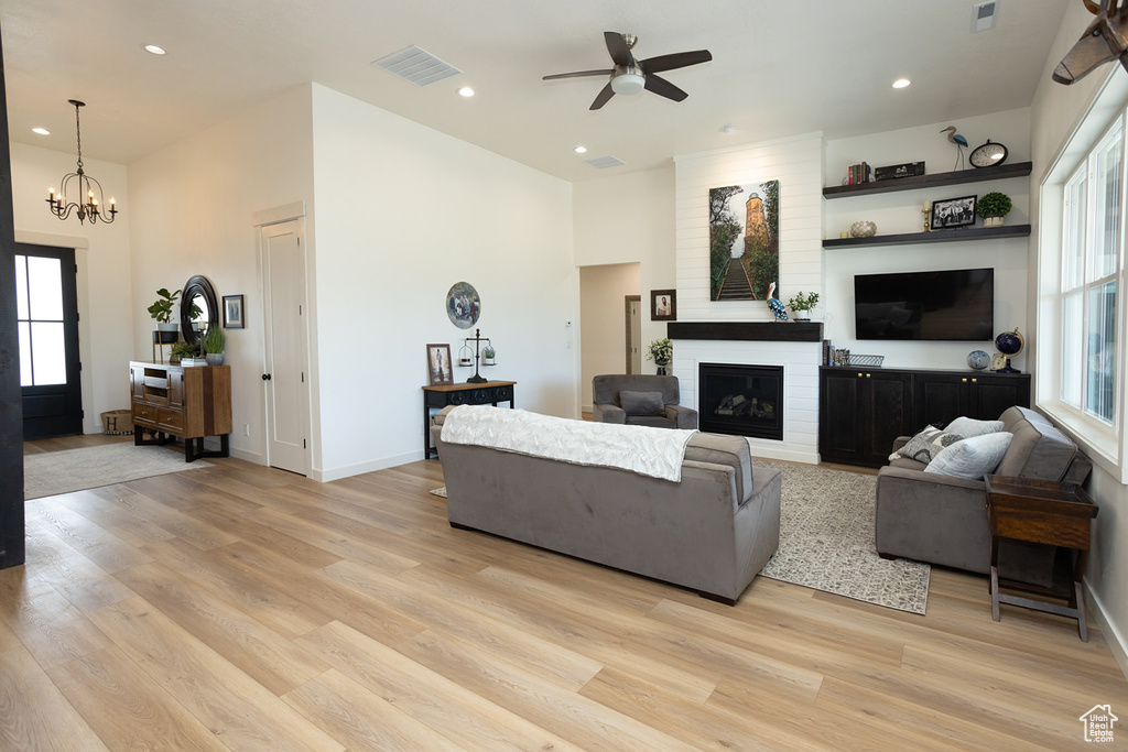 Living room featuring brick wall, a fireplace, light wood-type flooring, and ceiling fan with notable chandelier