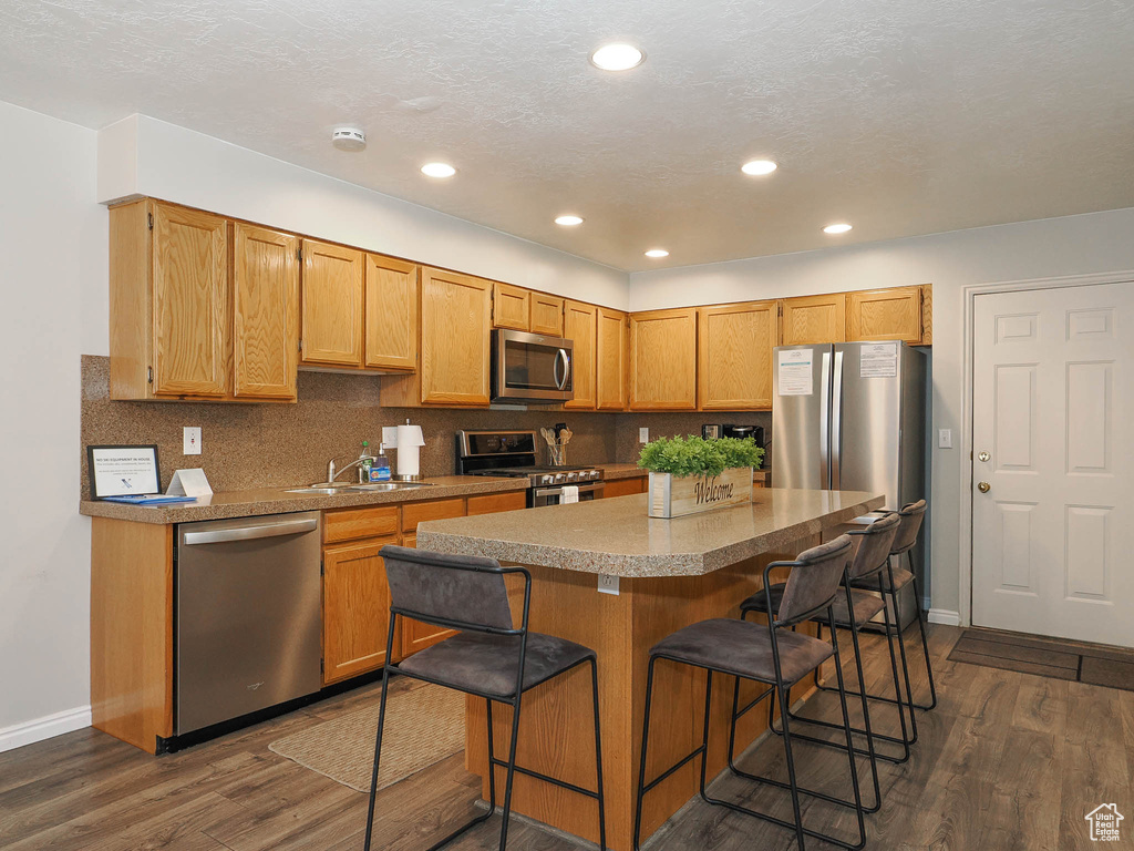 Kitchen with appliances with stainless steel finishes, a kitchen breakfast bar, tasteful backsplash, and dark hardwood / wood-style flooring