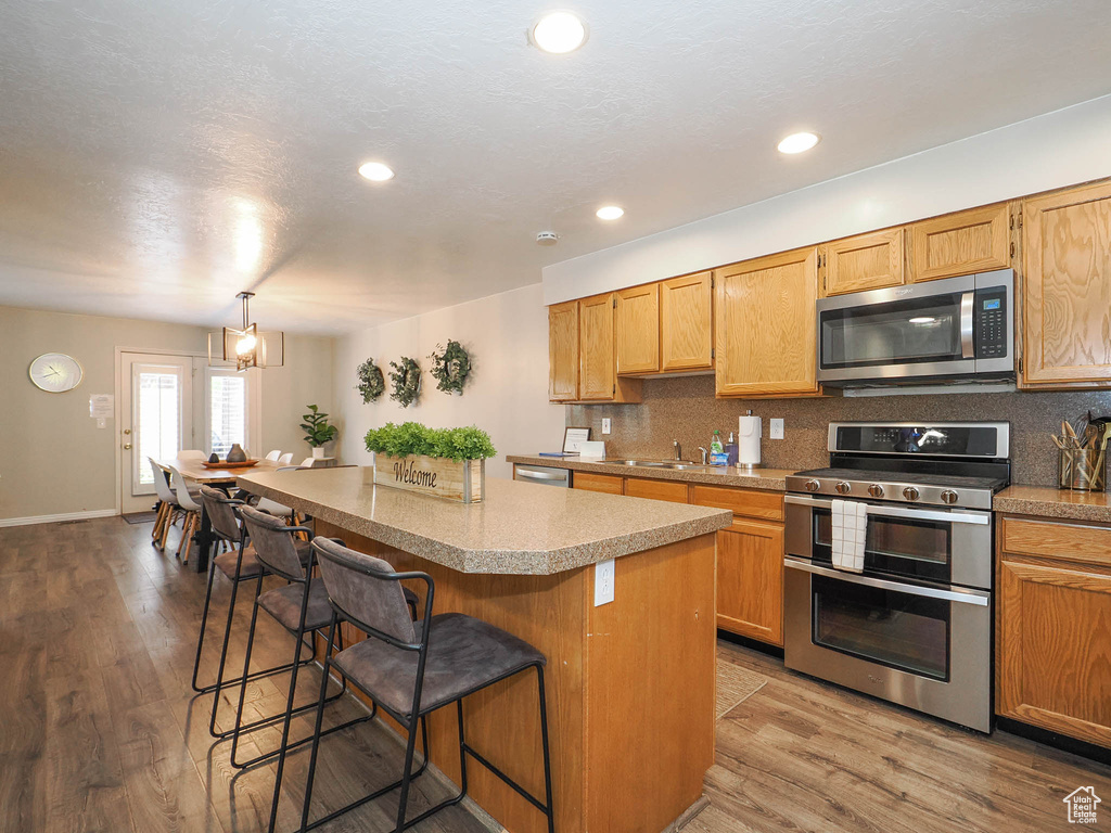 Kitchen with hardwood / wood-style floors, tasteful backsplash, stainless steel appliances, a kitchen island, and a breakfast bar